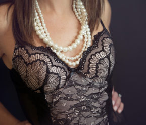 Model exhibits her black dress and pearl necklace
